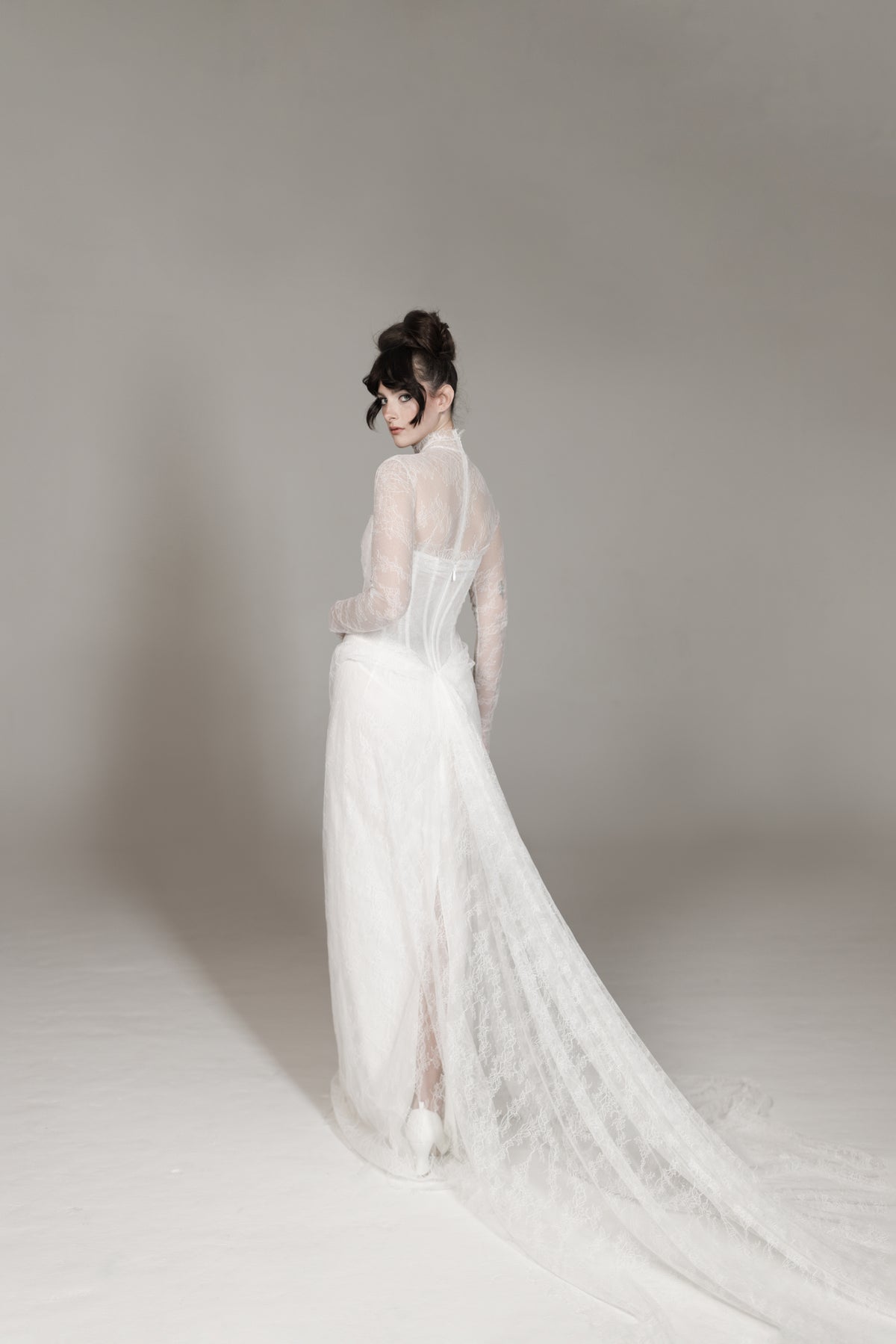 Woman in a white wedding dress standing against a plain background