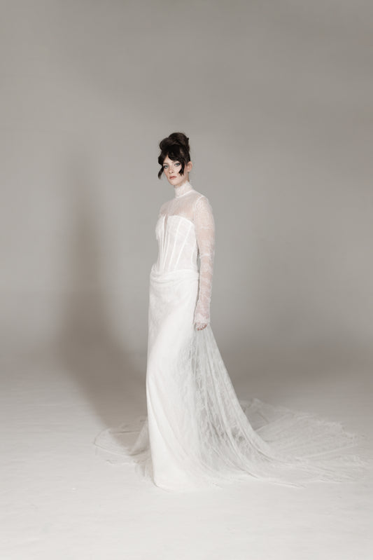 Woman in a white wedding dress standing against a plain background