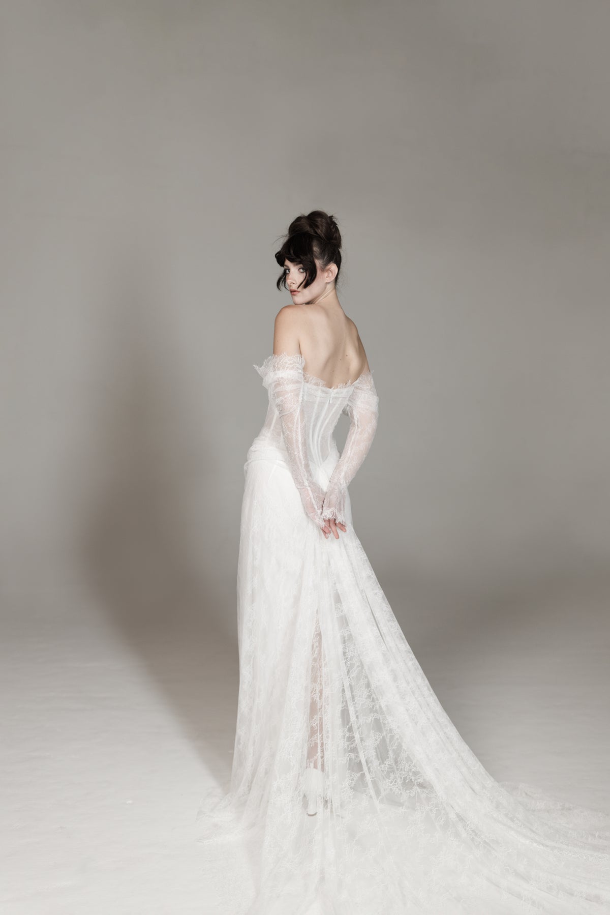 Woman in a white wedding dress with long sleeves and a flowing train against a plain background