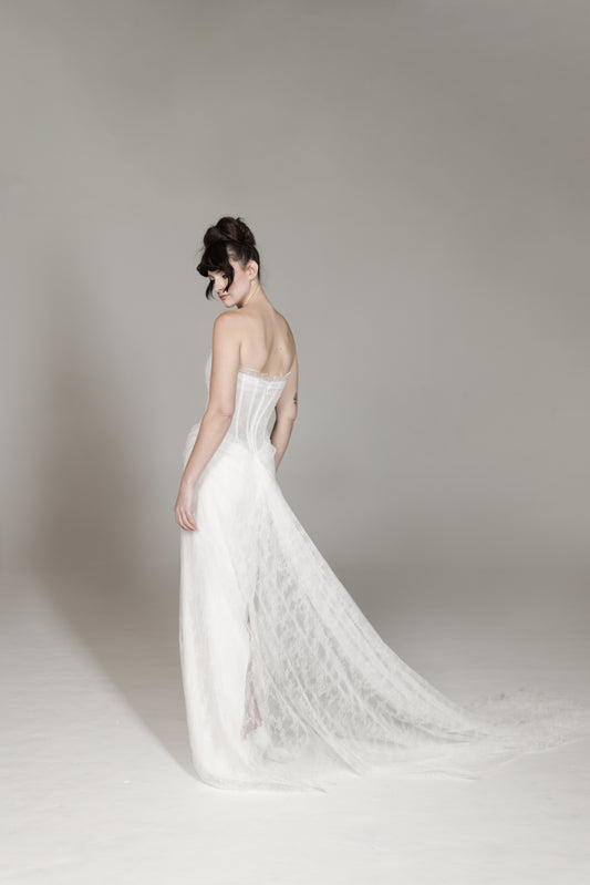 Woman wearing a white strapless gown with a long train on a plain background