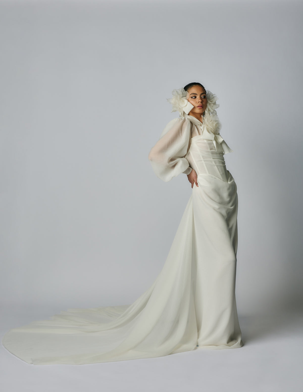 Woman wearing a long, elegant white dress with a flowing train on a plain background