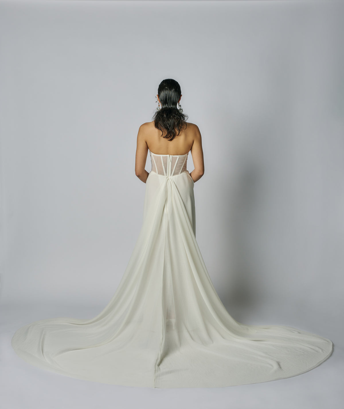 Woman wearing a white strapless gown with a long train on a gray background