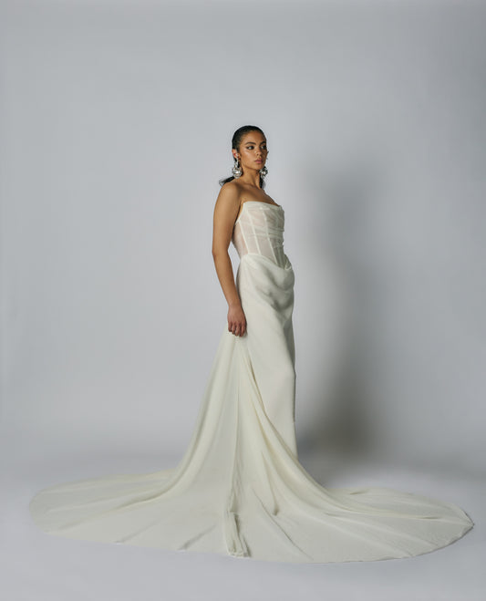 Woman wearing a strapless white wedding gown with a long train on a plain background
