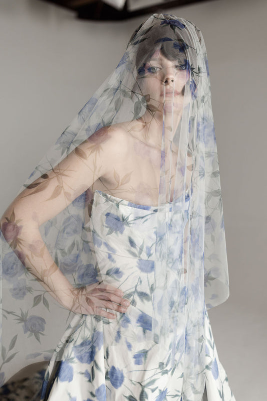 Woman wearing a floral dress and matching veil against a plain background