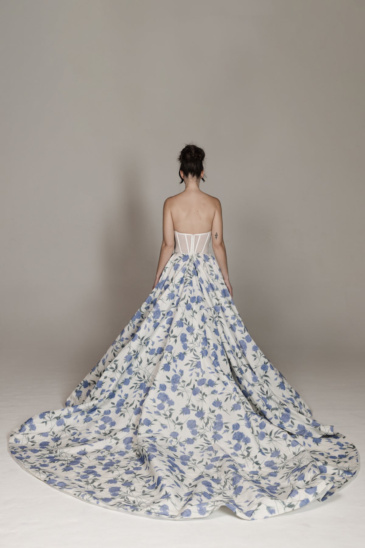 Woman wearing a strapless floral gown with a long train against a plain background