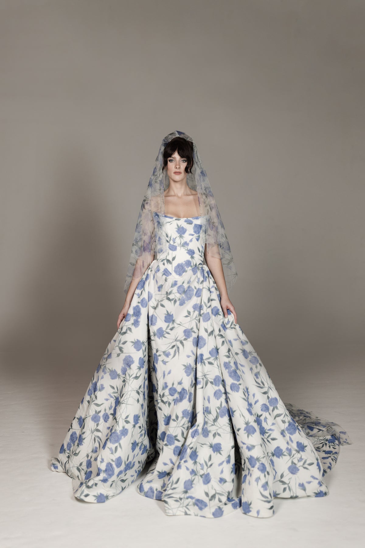 Woman wearing a floral wedding dress with a veil against a neutral background