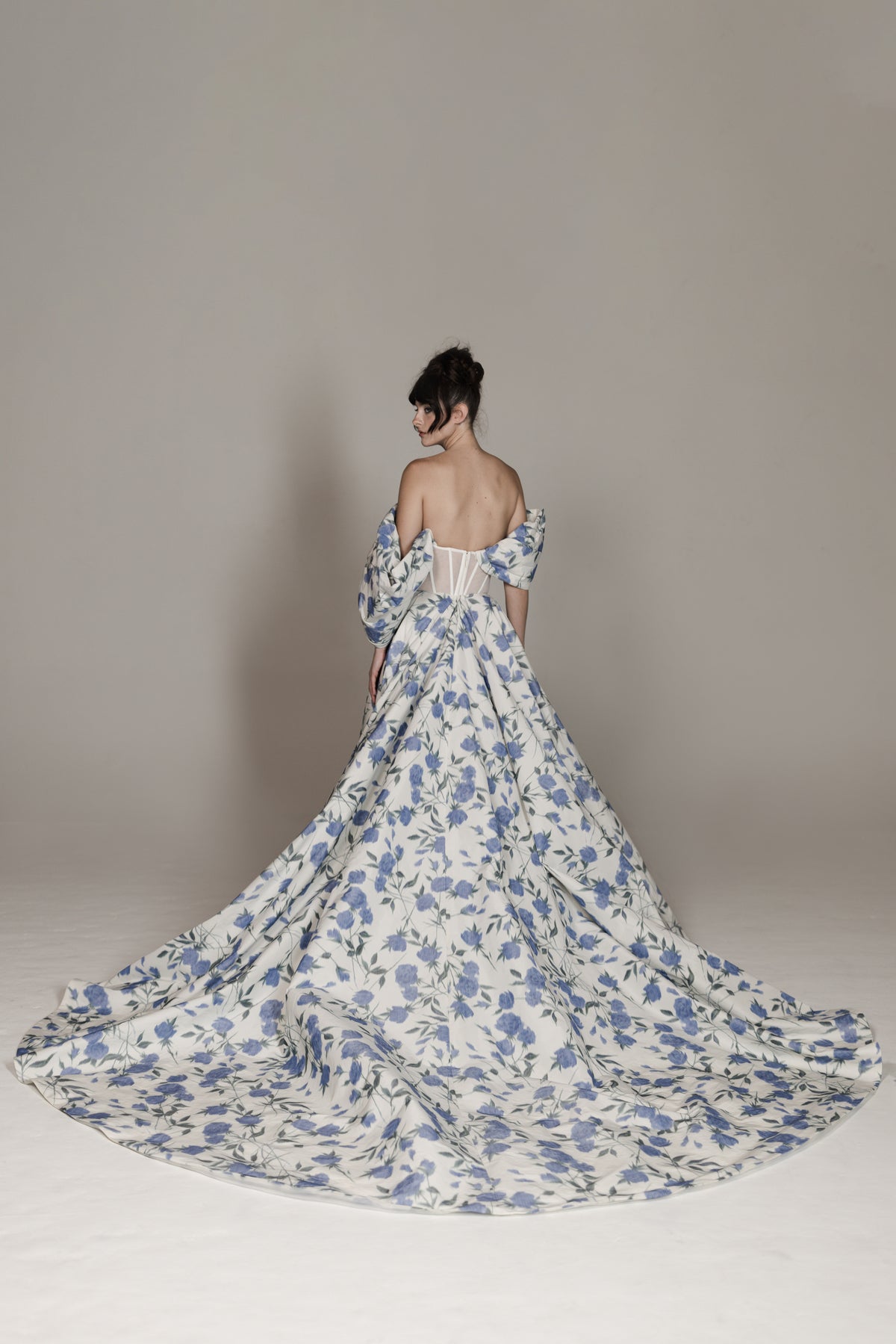 Woman wearing a floral off-shoulder gown with a long train on a plain background