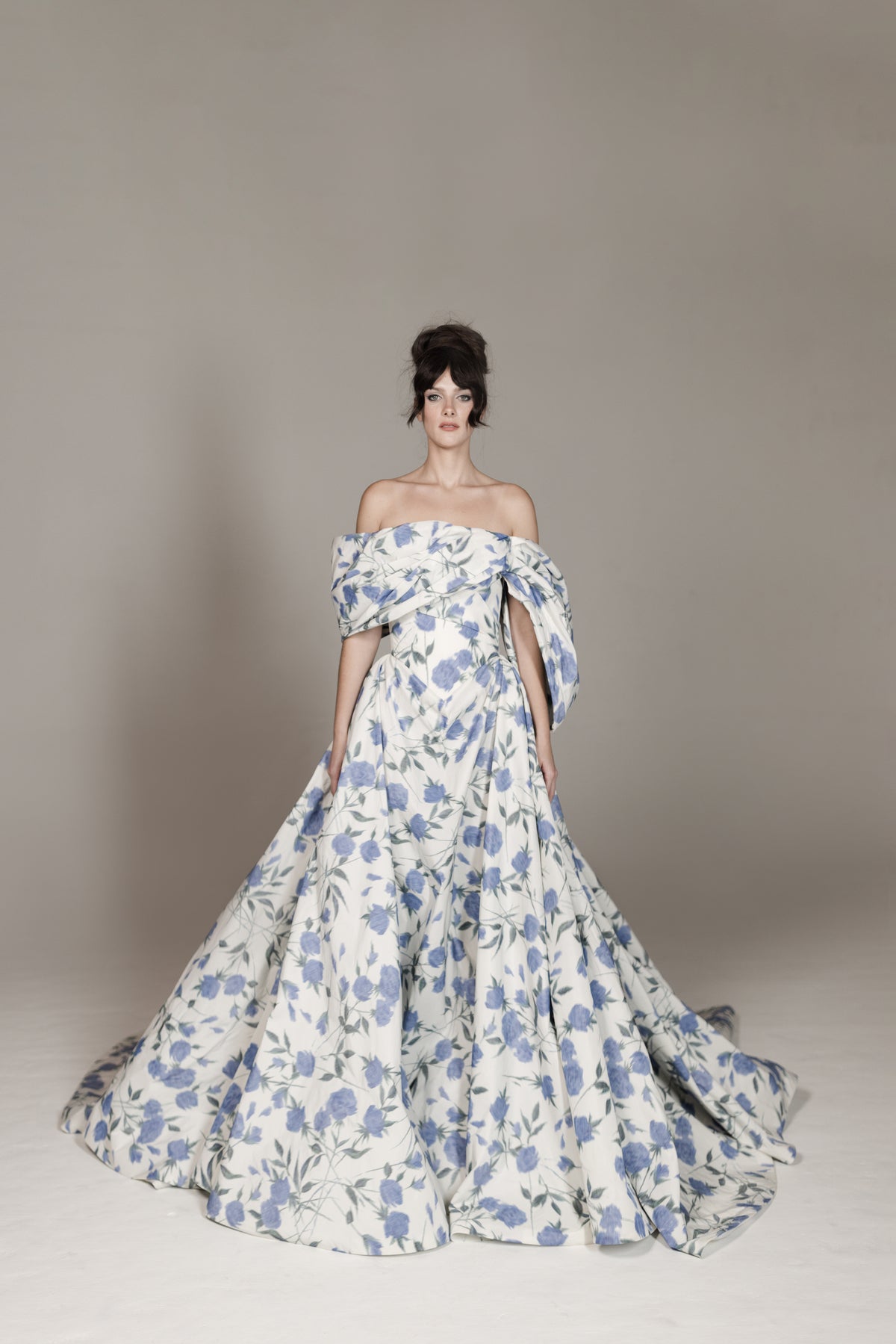 Woman wearing a floral off-shoulder gown against a plain background