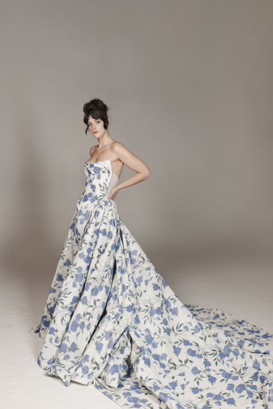 Woman wearing a strapless floral gown against a plain background