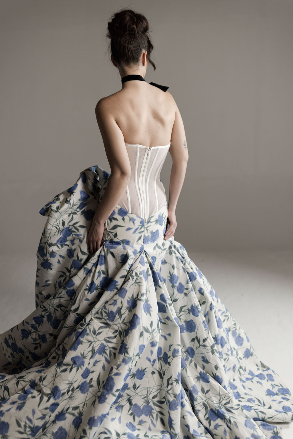 Woman wearing a white corset and floral gown against a plain background