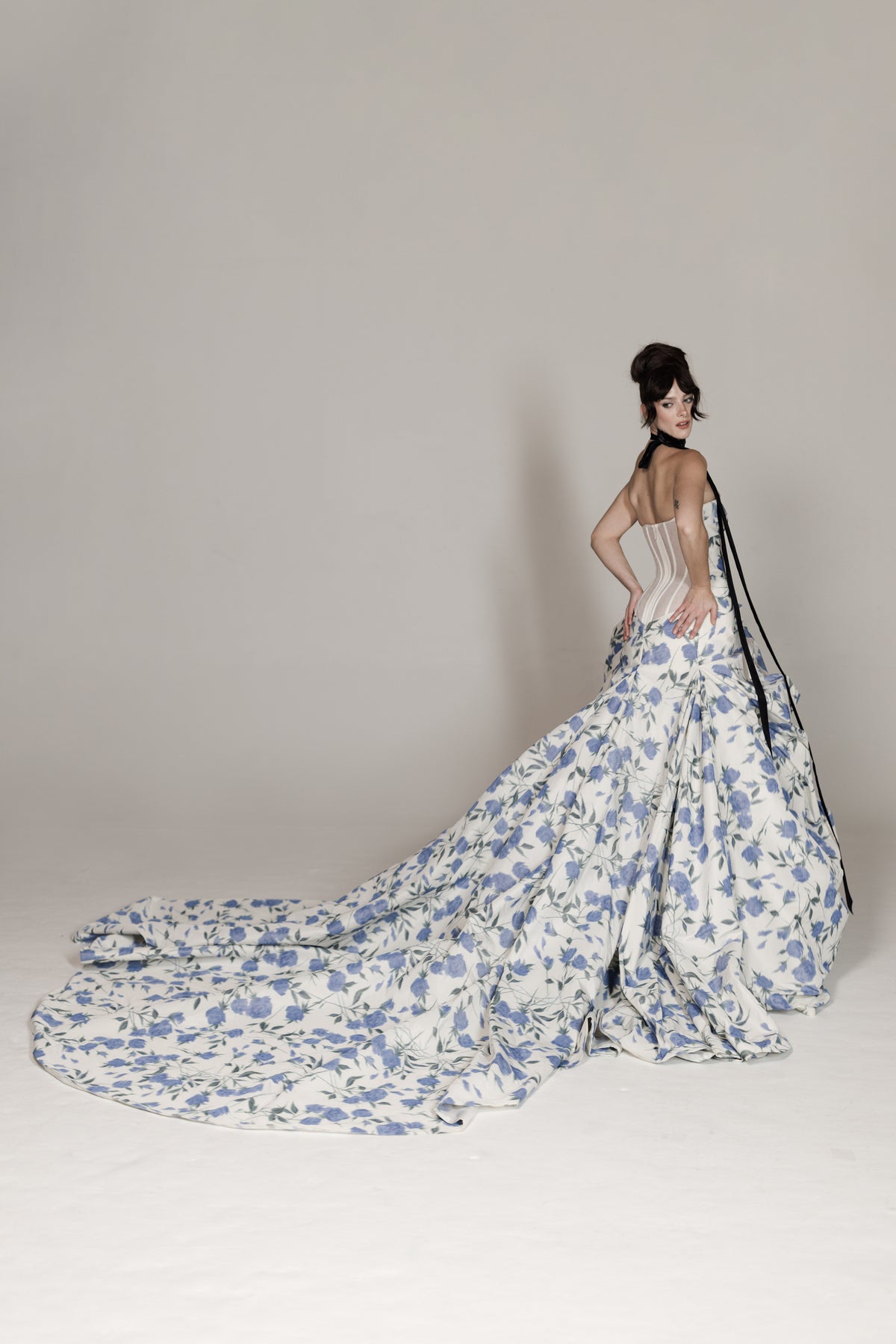 Woman wearing a floral gown with a long train on a plain background