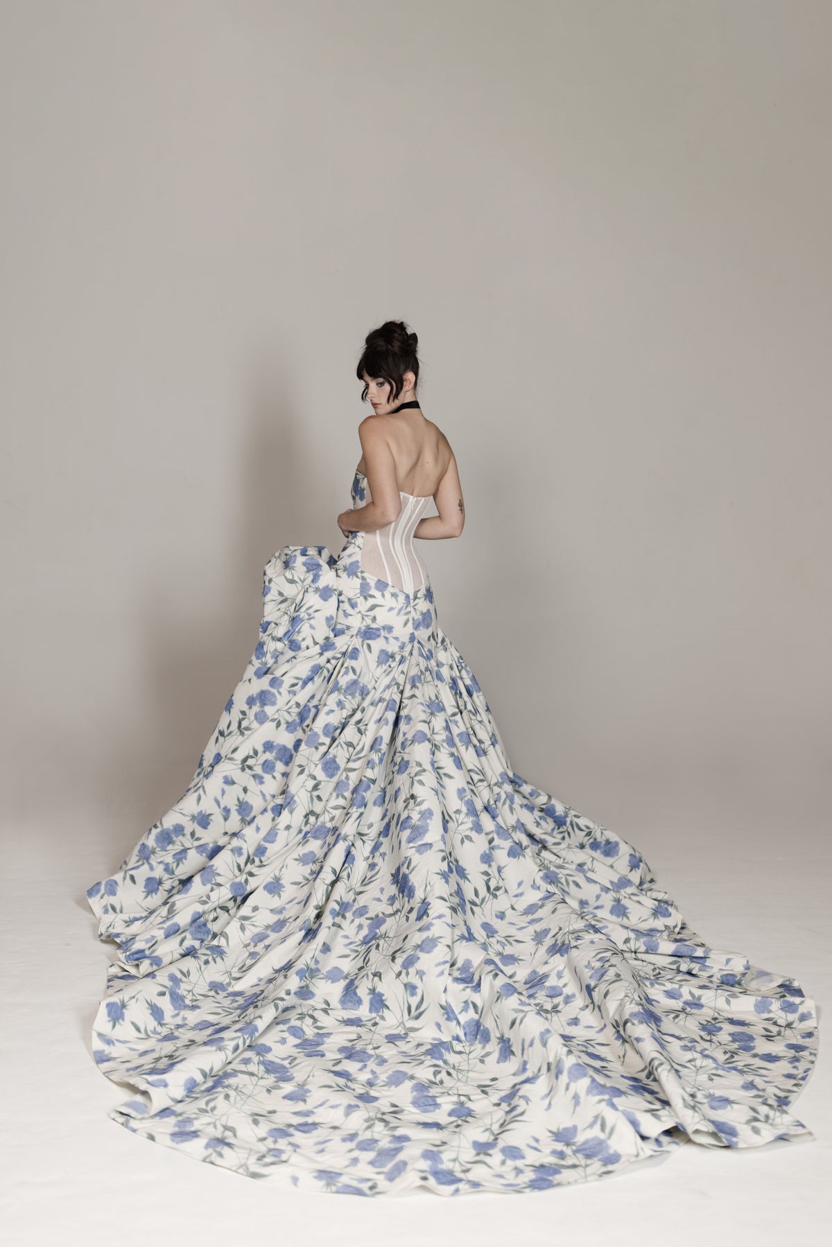 Woman wearing a floral gown with a long train on a plain background