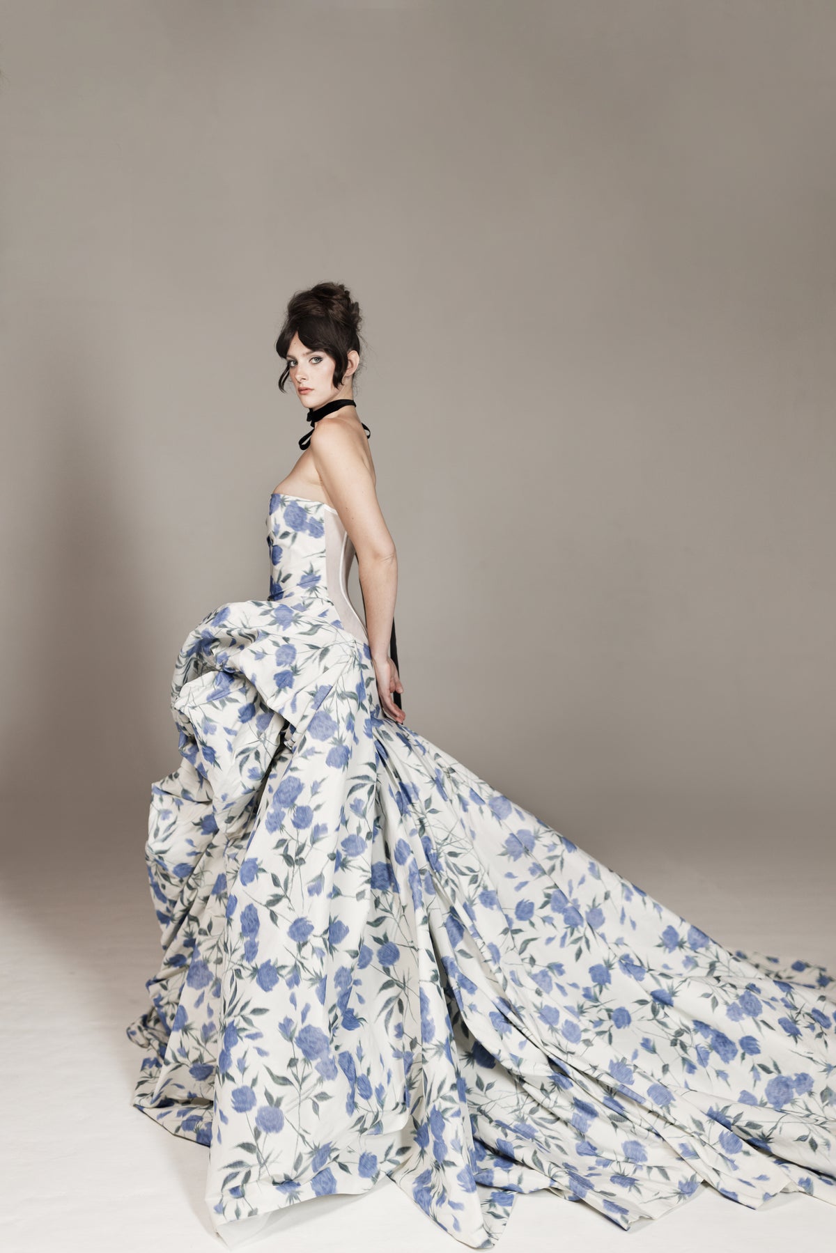 Woman wearing a floral strapless gown with a long train on a plain background