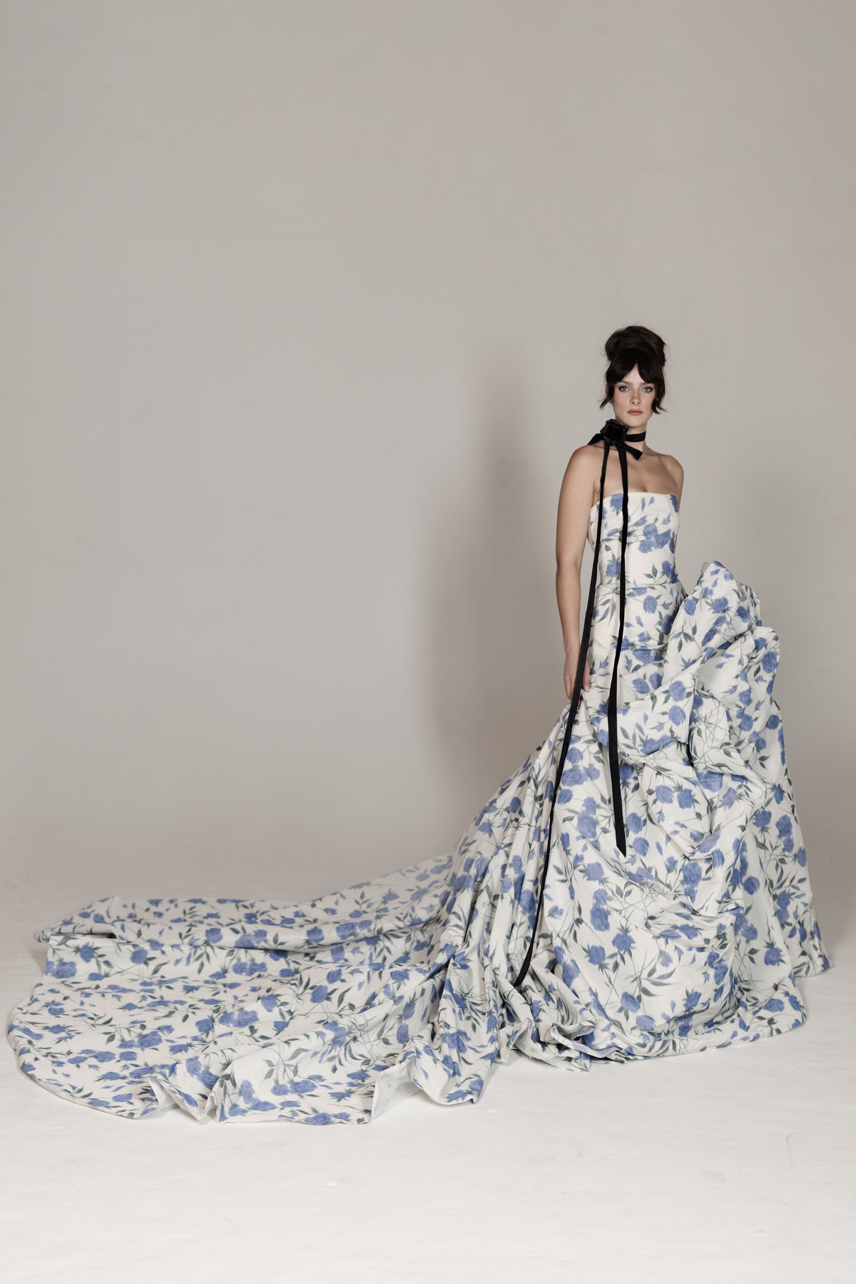 Woman wearing a floral gown with a long train on a plain background
