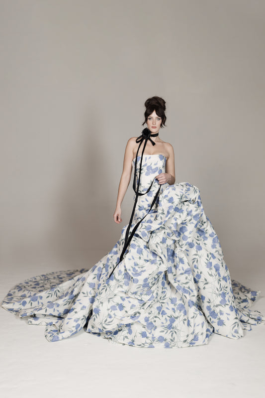 Woman wearing a floral gown with a long train on a plain background