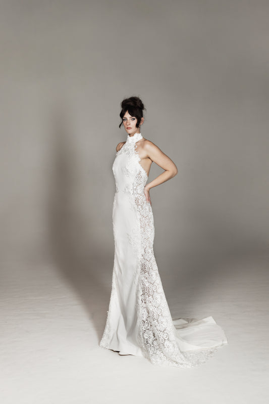 Woman wearing a white wedding dress with floral details on a plain background