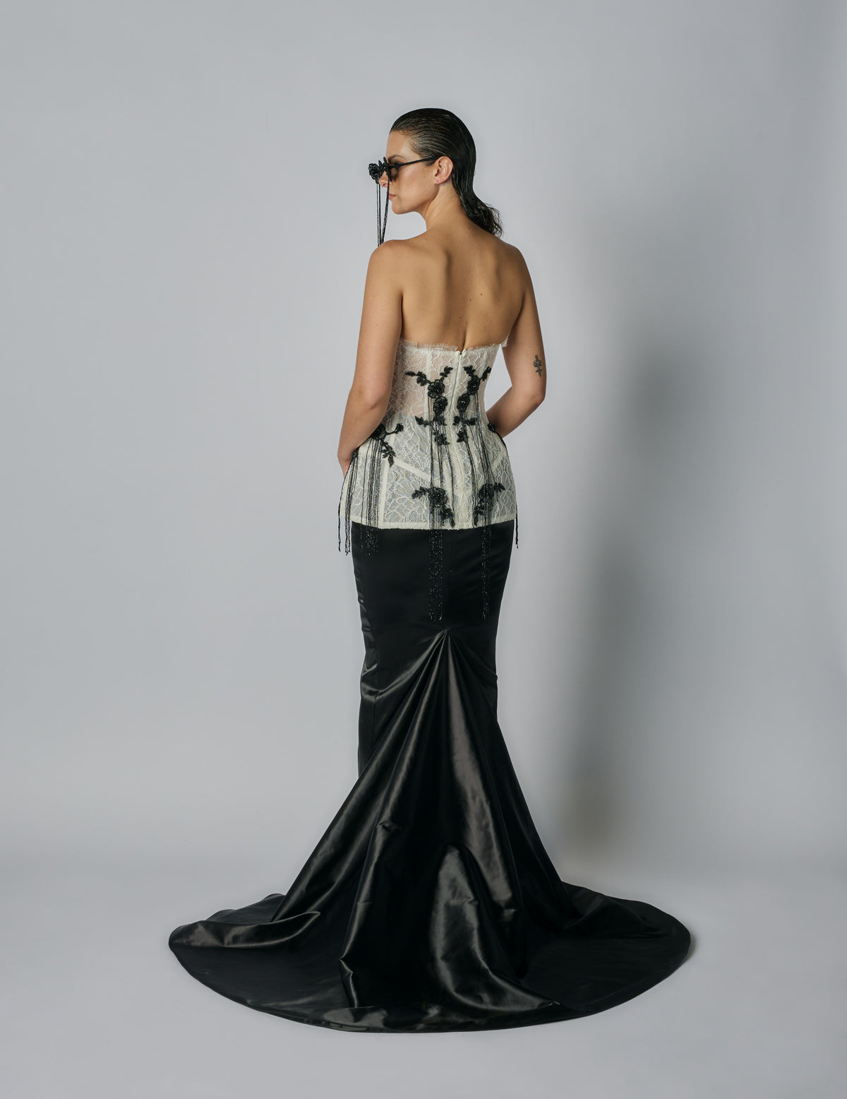 Woman wearing a strapless top with black floral patterns and a long black skirt on a plain background