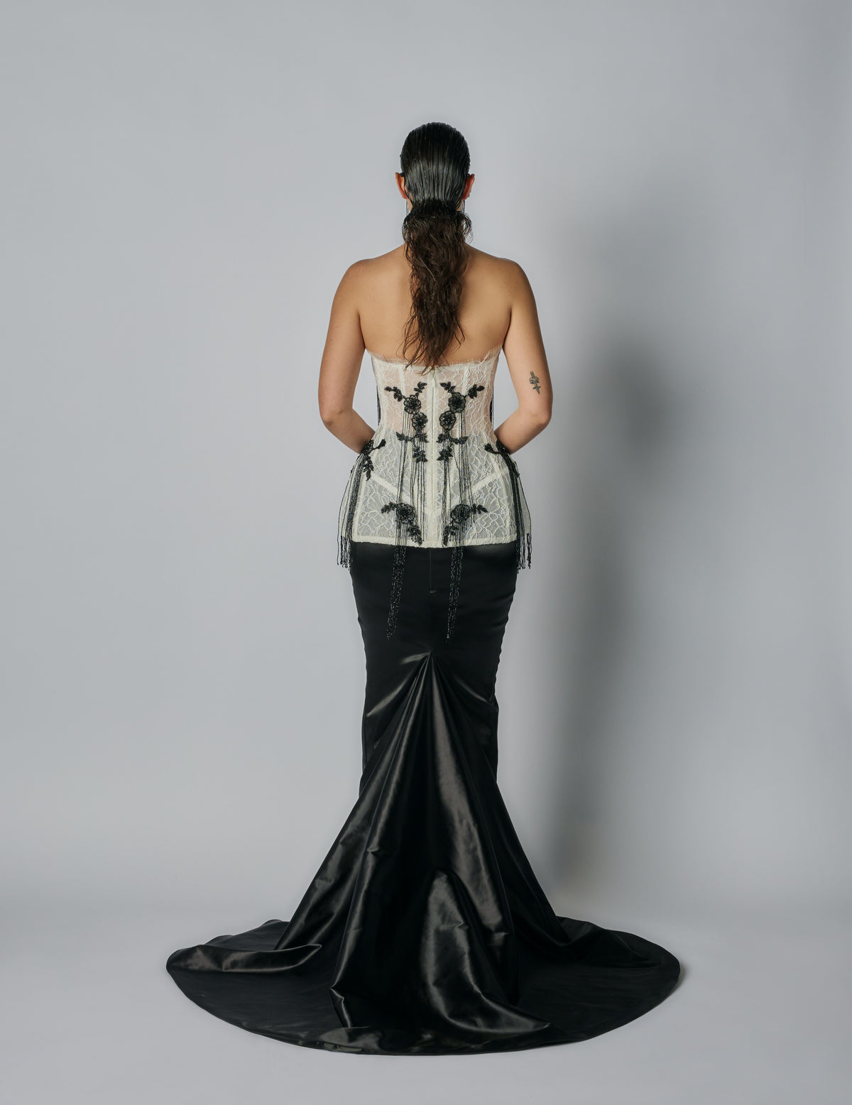Person wearing a strapless top with floral embroidery and a black satin skirt on a plain background