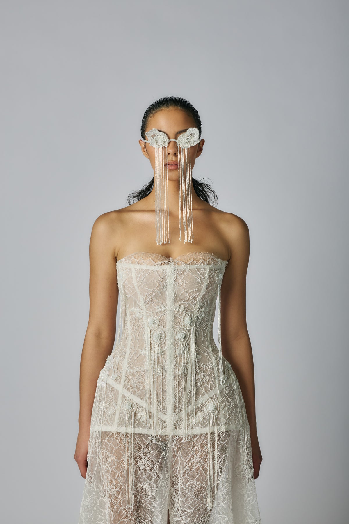 Model wearing a strapless lace dress with a sheer face veil against a gray background