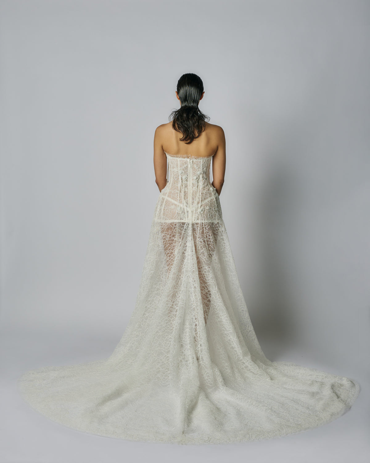 Woman wearing a strapless lace wedding dress on a plain background