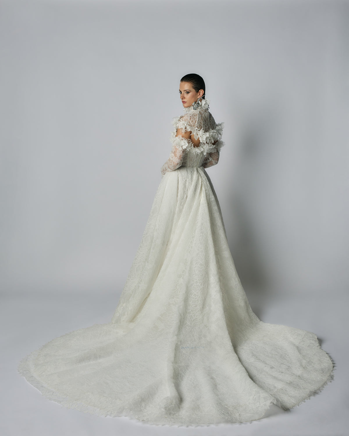 Woman wearing a white wedding dress with a long train on a plain background