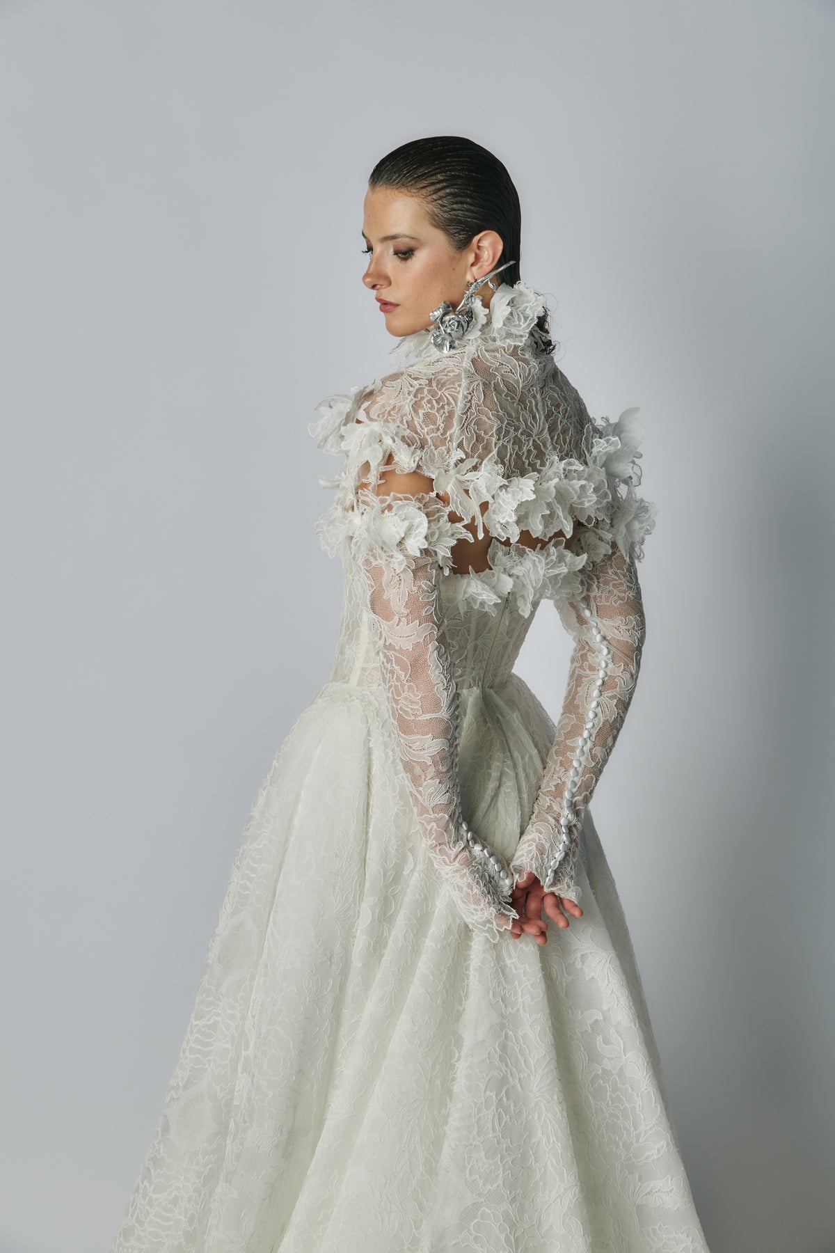 Woman wearing a white lace wedding dress with floral details on a gray background
