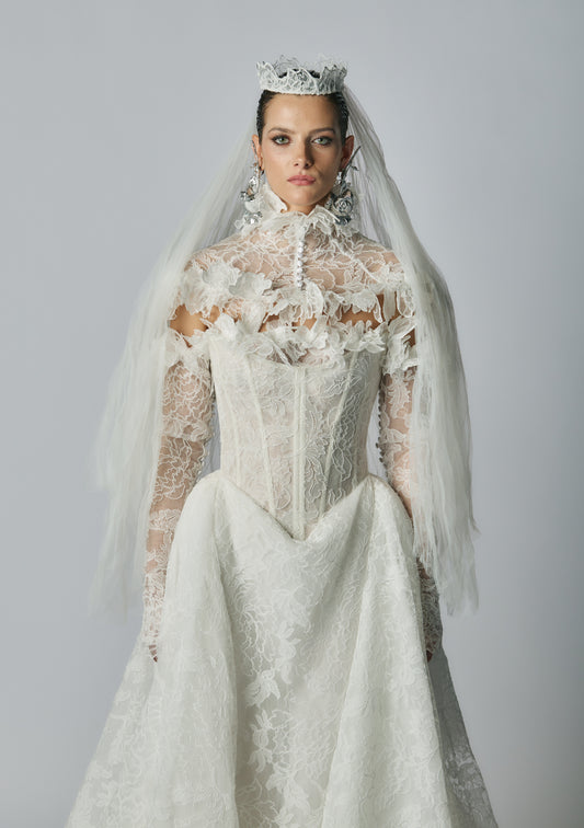 Woman wearing a detailed white wedding dress with a veil and tiara on a gray background
