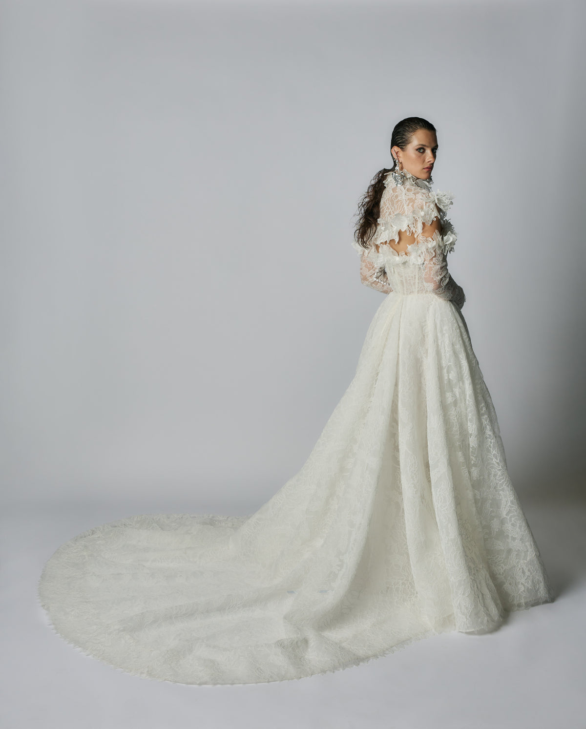 Woman wearing a white lace wedding dress with a long train on a plain background
