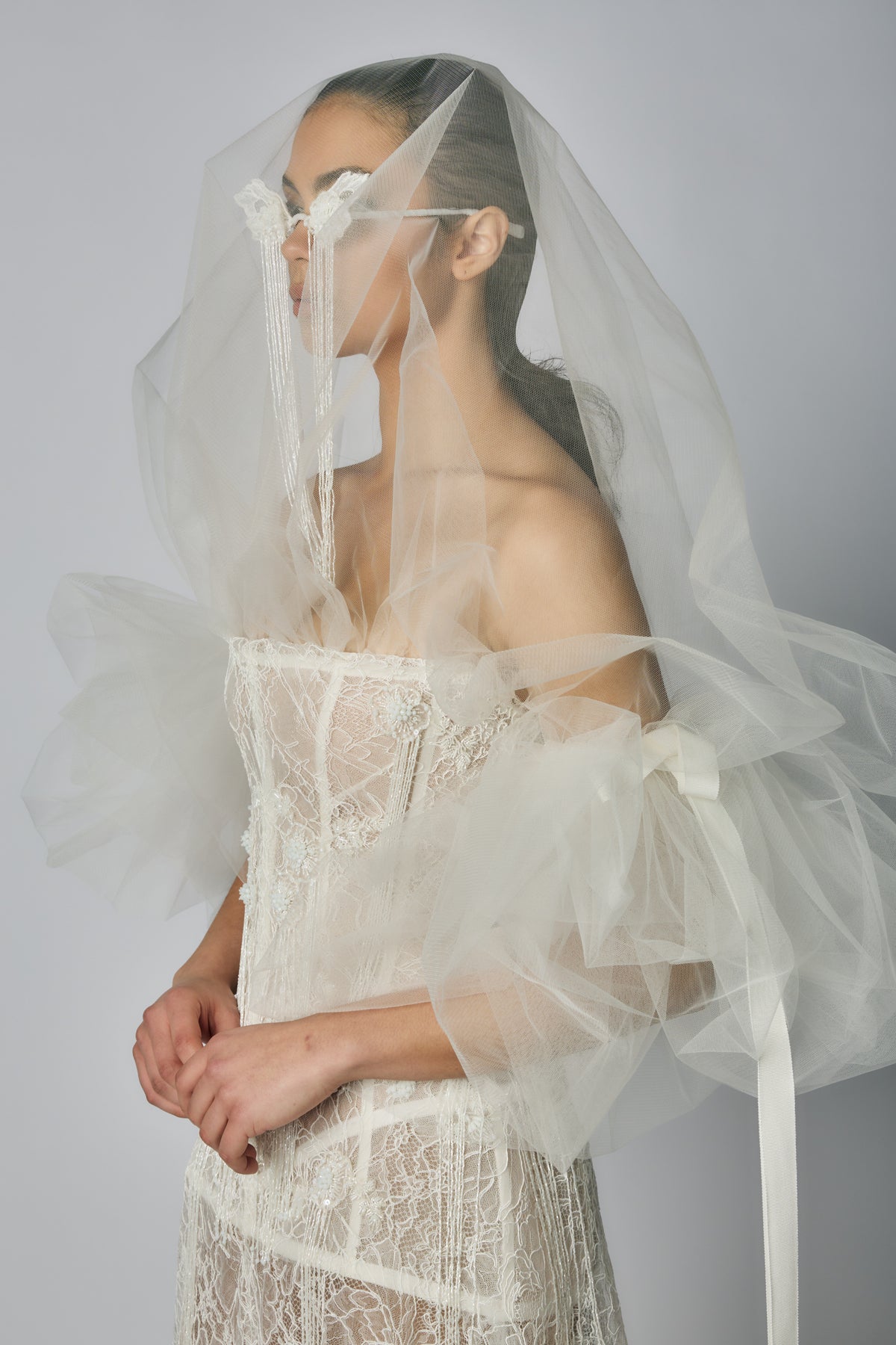 Woman wearing a white lace dress and veil against a plain background