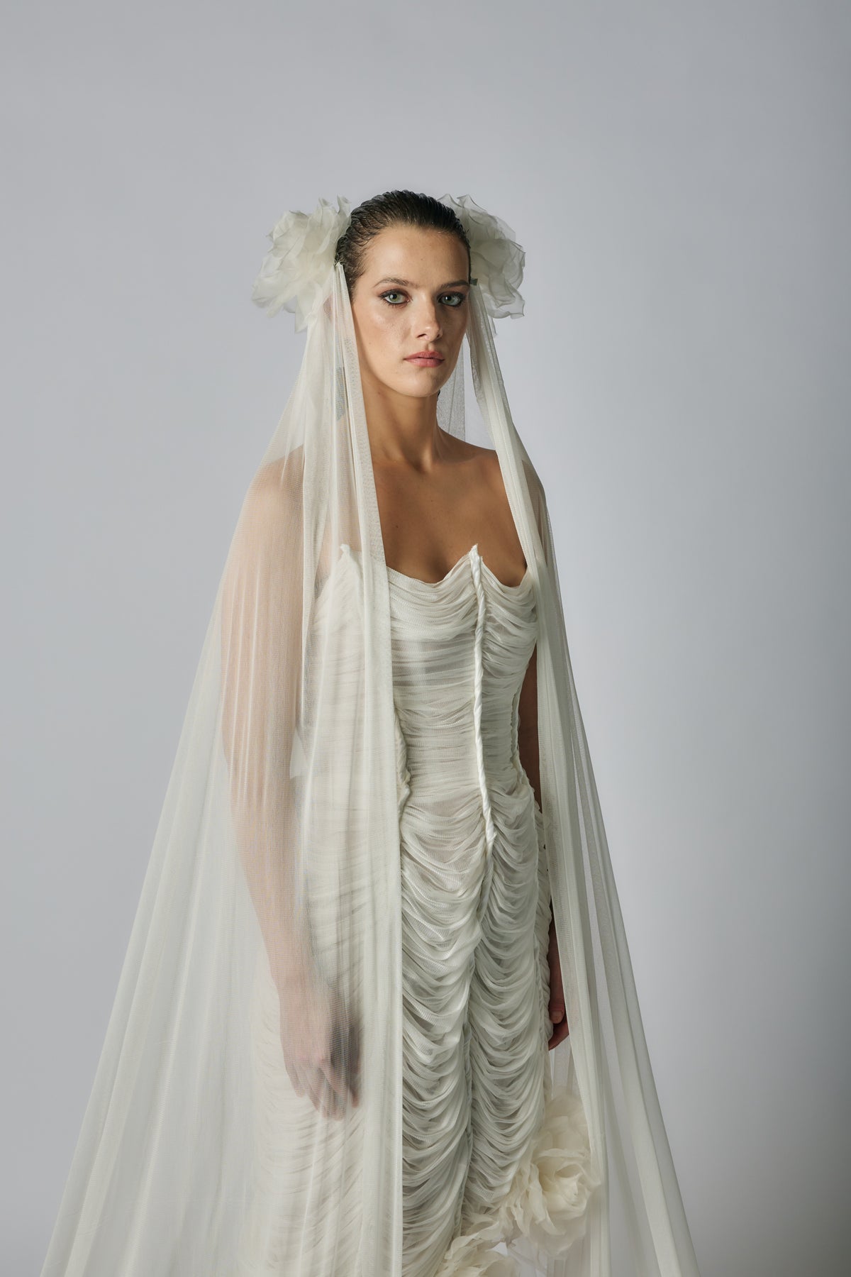 Woman wearing a white wedding dress with a long veil against a gray background