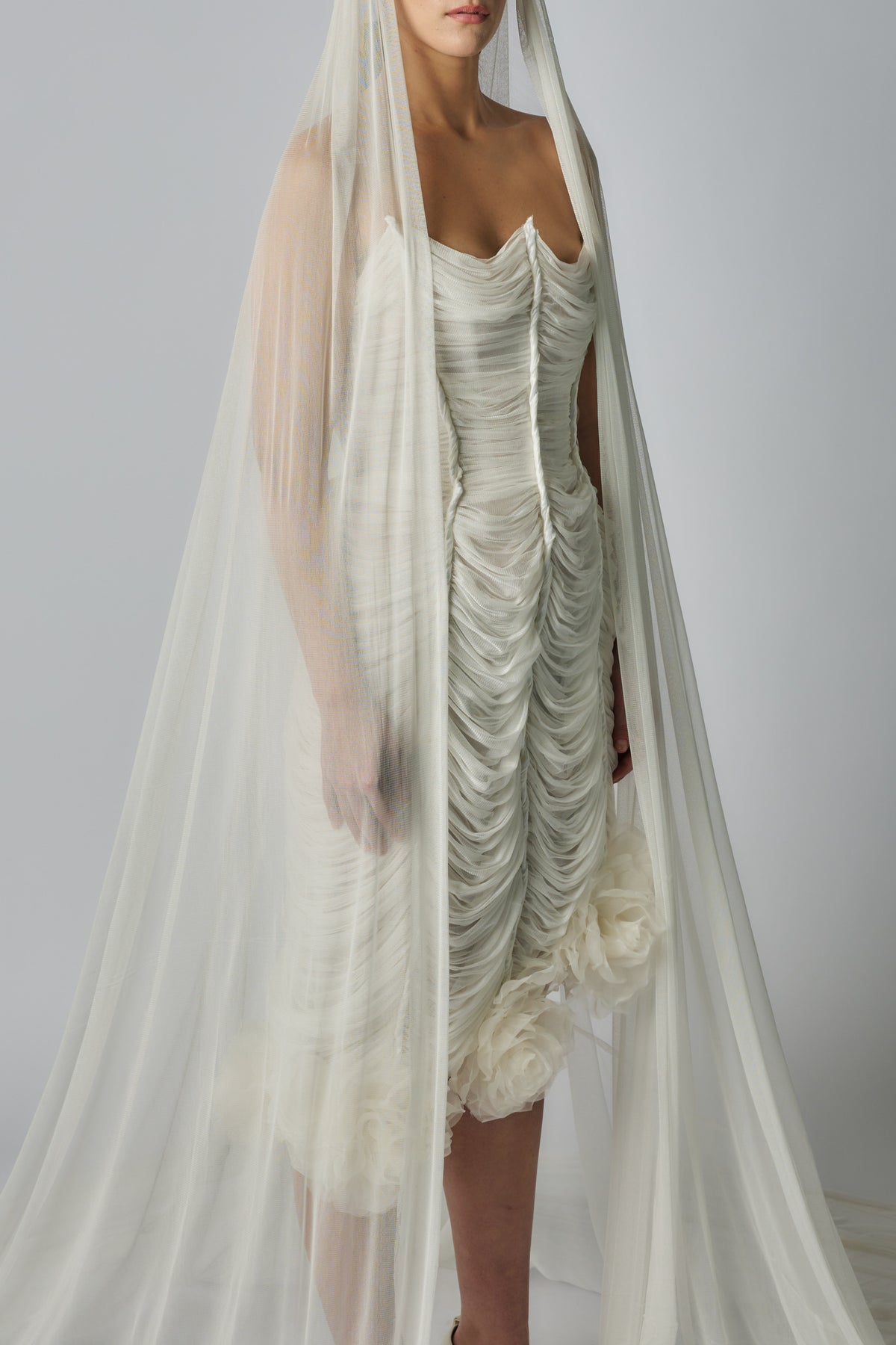 Woman wearing a white strapless dress with a long sheer veil against a plain background